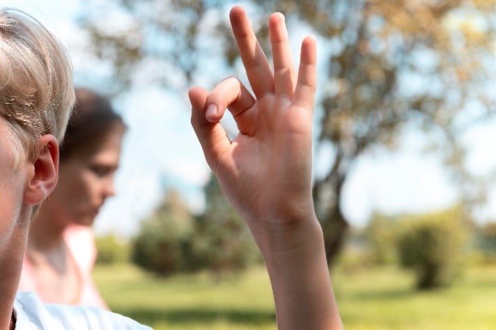 Un enfant écoute. On voit seulement son oreille et un signe qu'il fait avec sa main.