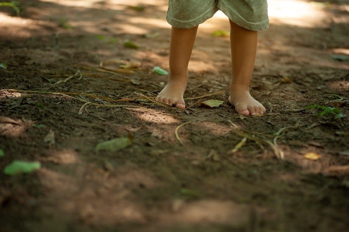 Jeune enfant qui marche pieds nus sur la terre. Seules ses jambes sont visibles.