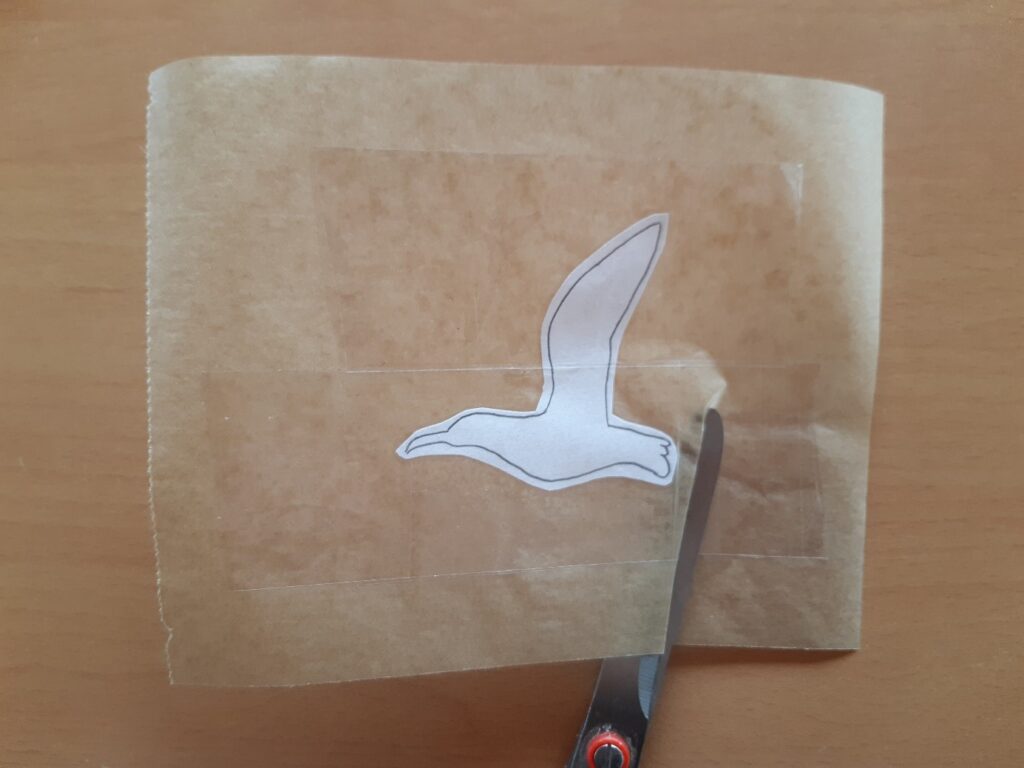 Découpe d'un autocollant d'oiseau en vol sur feuille de papier cuisson sur une table en bois.