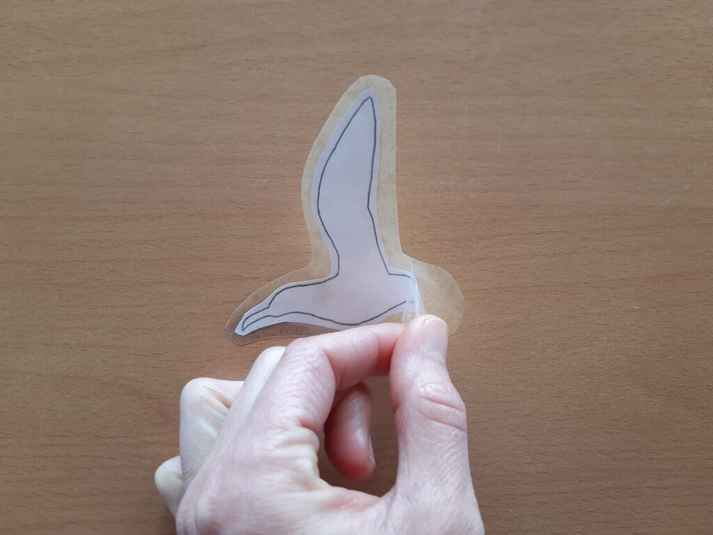 Autocollant contour d'oiseau prêt à être collé. Main en avant plan.