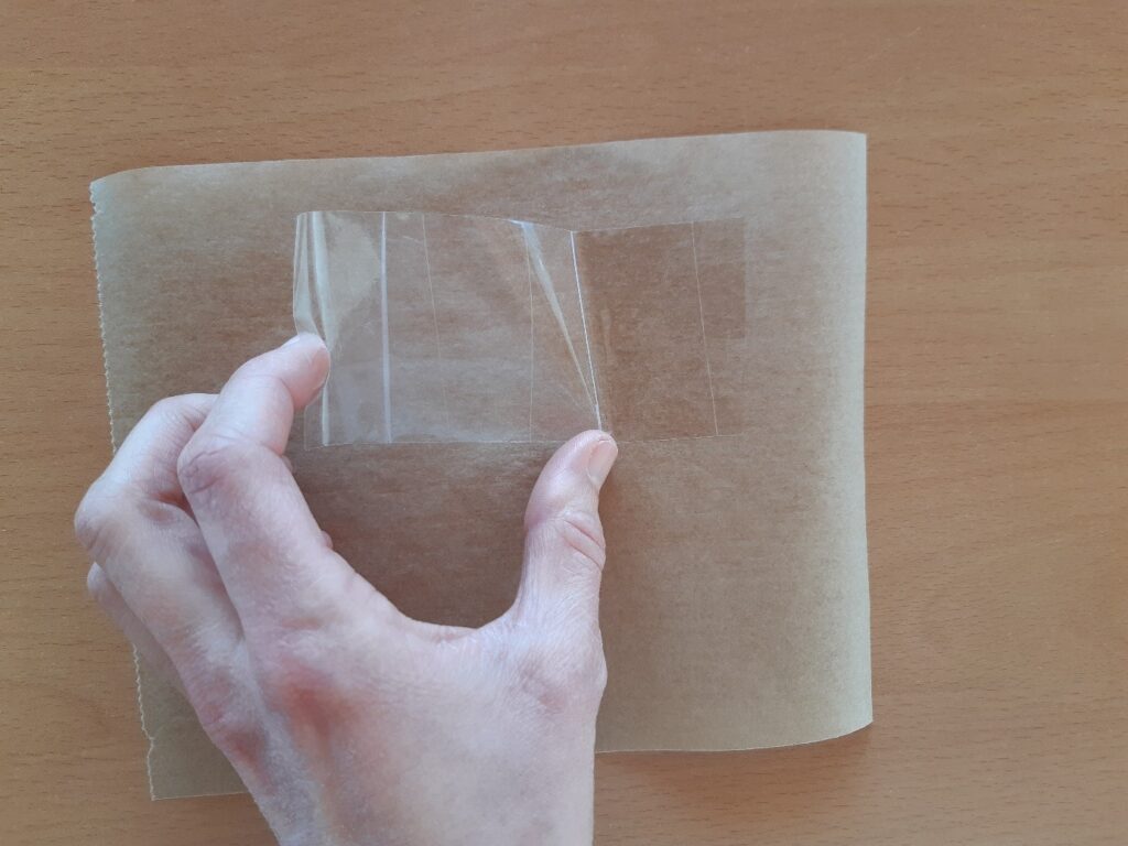 Bout de scotch déposé sur une feuille de papier cuisson par une main.