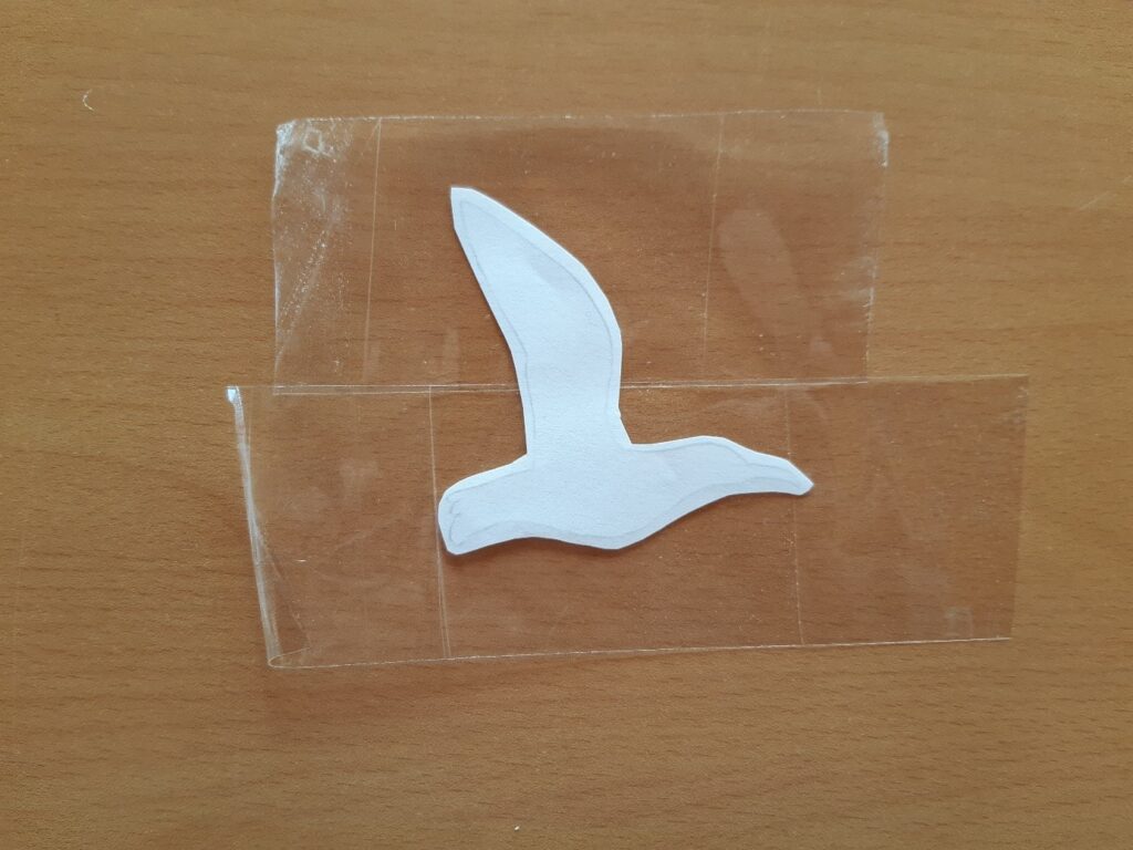 Contour du dessin d'oiseau posé sur des bouts de scotchs eux-mêmes posés sur une table en bois.