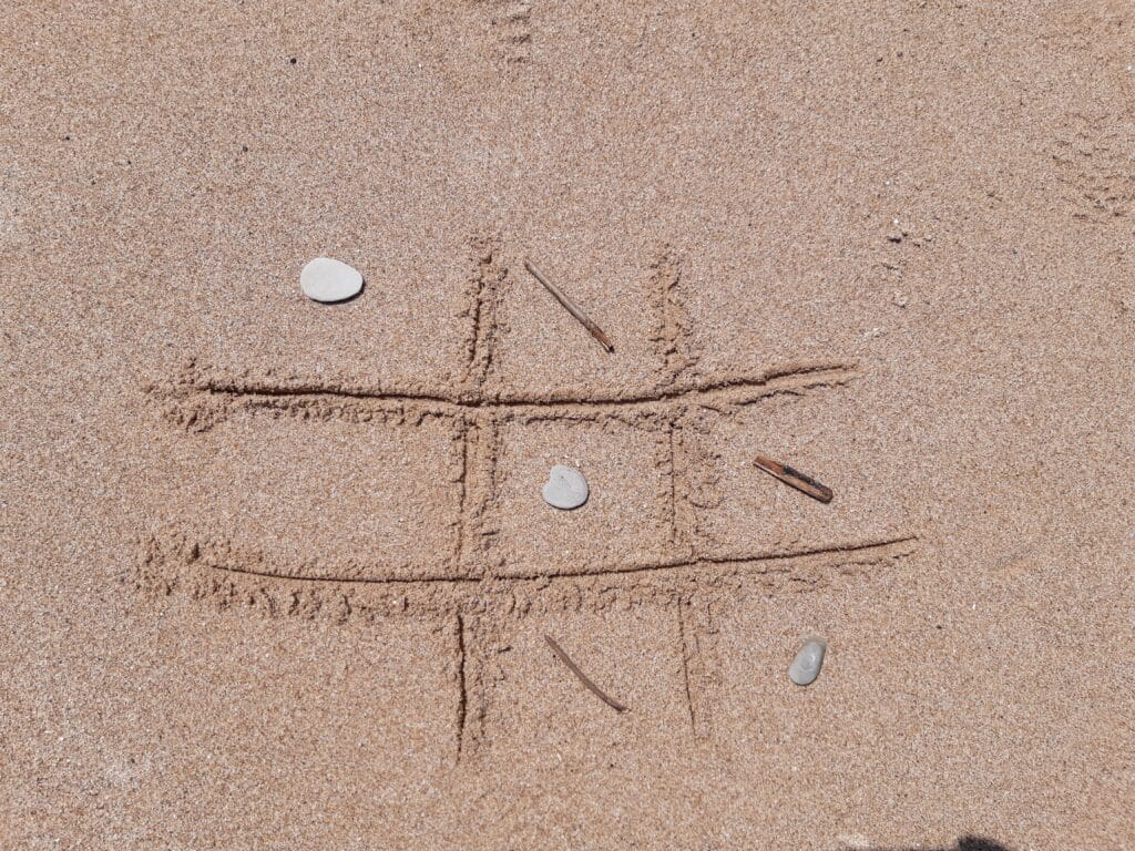 Jeu du morpion dessiné dans le sable : des bâtons et cailloux servent de pions.