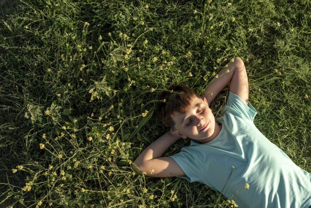 Enfant souriant allongé dans l'herbe les mains posés sous sa tête.