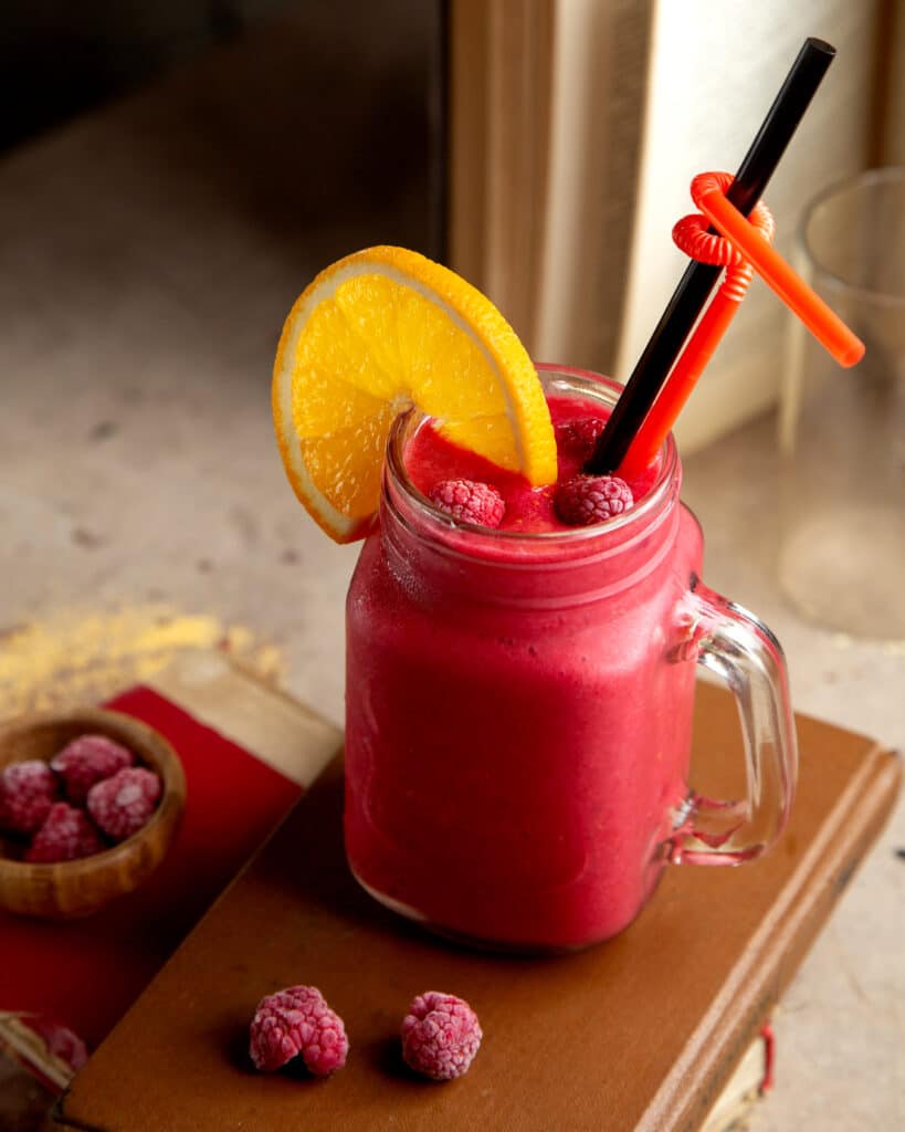 Smoothie fruits rouges, paille, framboises et tranches d'orange en décoration