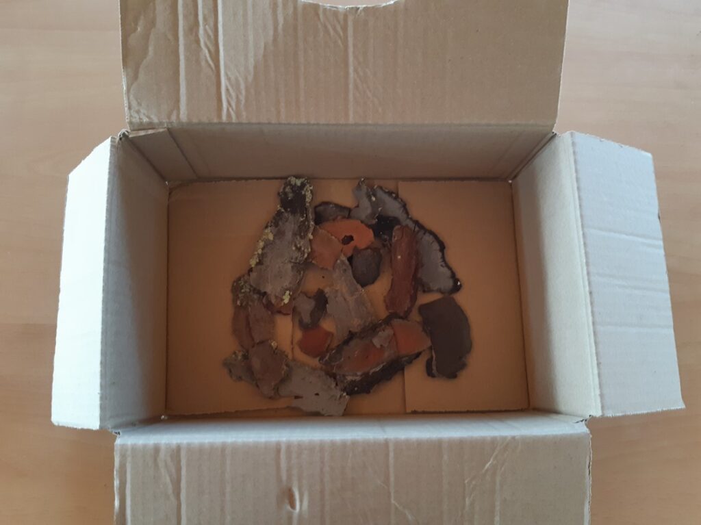 Boîte en carton ouverte avec des bouts d'écorce d'arbres dedans.