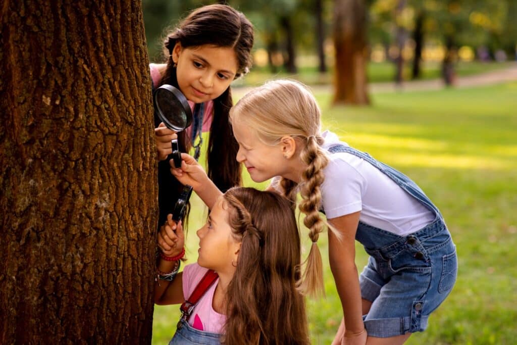 Trois petites filles observent un tronc d'arbre avec des loupes.