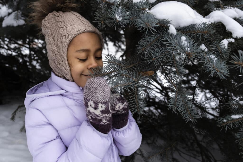 Jeune fille qui sent un sapin en hiver. Il y a de la neige.